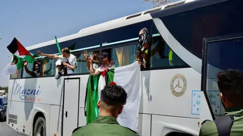 Getty Images Activists lean out of the side of a bus waving Palestinian and Algerian flags.