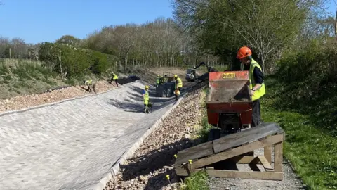 Shropshire Union Canal Society Six people in yellow high-visibility yellow jackets working on a concrete canal bed.