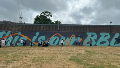 People painting a mural with inscription "This is our BBL" and a blackbird at the end.