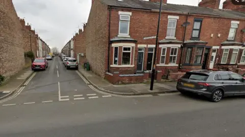 Parked cars close to a street junction alongside terraced homes. 