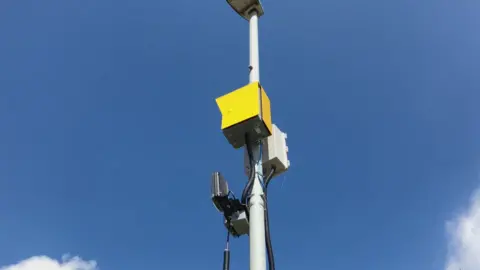 BBC/Seb Cheer A yellow box attached to a lamp post with two sensors underneath it.