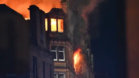 A sandstone building on fire at night with flames bursting through the windows