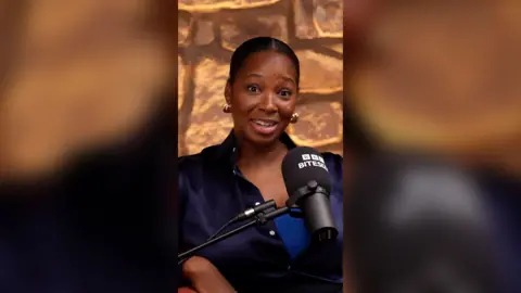 Jamelia looks at the camera. She's wearing a navy shirt that's unbuttoned and has a surprised expression.
