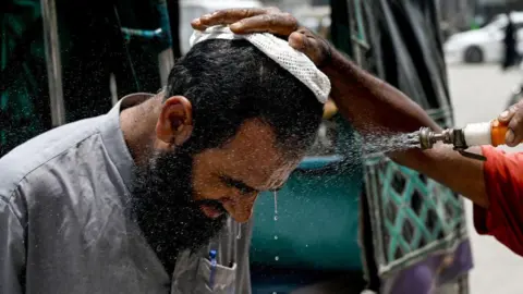 Getty Images In Karachi, a volunteer sprays water on a bypasser's face to cool off during a hot summer day