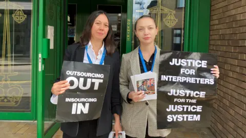 Two interpreters holding signs including "justice for interpreters" and "outsourcing out, insourcing in"