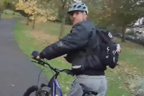 A photo of the man police want to trace in connection with the incident. He is wearing a bike helmet and a black jacket, with a black bag pack. He is also pushing a dark-coloured bike.