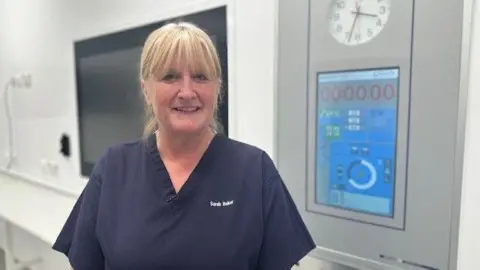 BBC/ Mark Denten A woman in navy scrubs stands in a temperature-controlled theatre.