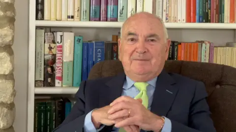 Man sat in chair in front of a bookcase