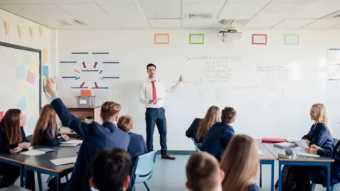 A school classroom with a teacher pointing to a white board 