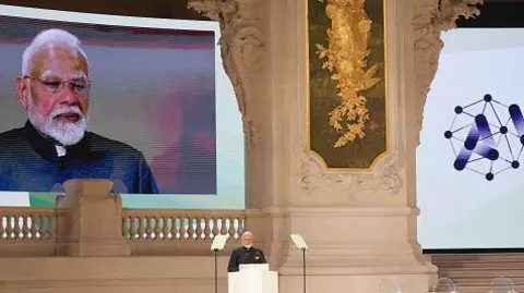 Getty Images The image shows Narendra Modi, India's prime minister, on the podium speaking at the AI Action Summit in Paris in February 2025. There's also a big screen live streaming his speech right behind the stage where he is standing. 