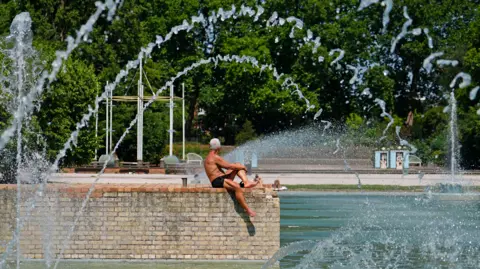 PA Media A man sunbathes next to the water in Battersea park