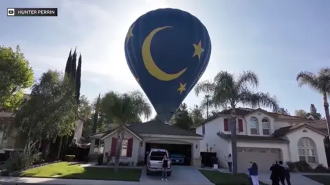 A blue hot air balloon lands in a backyard.