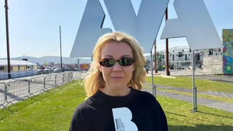 A woman with blonde hair is wearing sunglasses and looking at the camera