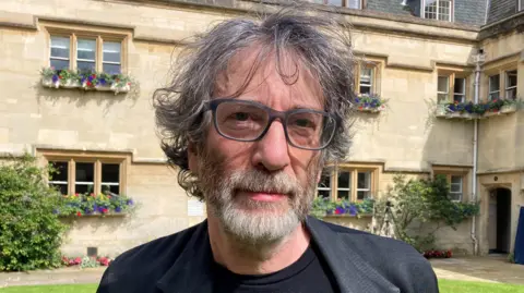 BBC Neil Gaiman wearing a black t-shirt and black jacket