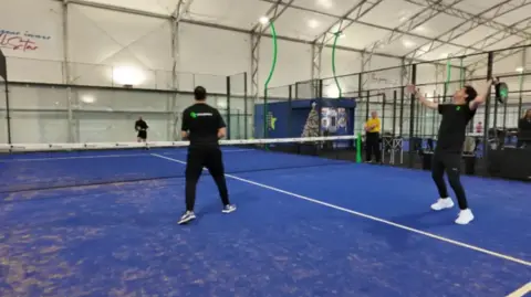 Three people playing padel on an indoor blue court