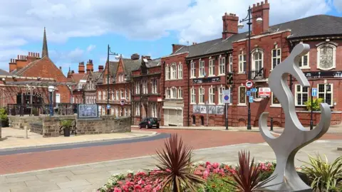 Stock image of Rotherham's town, with an array of different buildings in a row and a metal statue