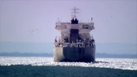 Shot from behind, a large cargo ship is stuck, surrounded by ice on Lake Erie