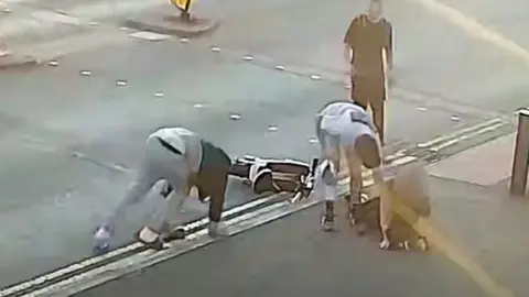 A group of people surround a woman who has been knocked over by an e-bike