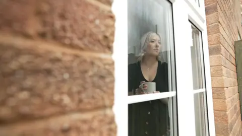 Jessica looks out the window of her home