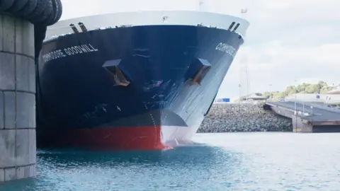 The front of the Commodore Goodwill boat coming into St Helier harbour. Clear skies behind and land.
