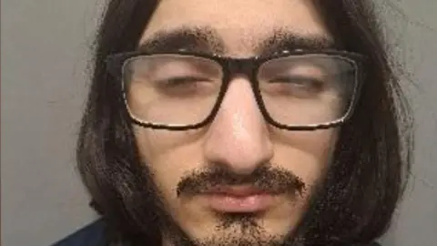A custody image shows a man with long hair and glasses
