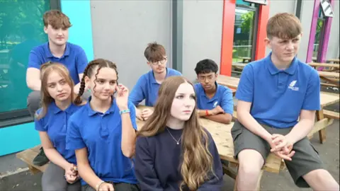 A group of teenagers sitting on a bench outside in the school premises
