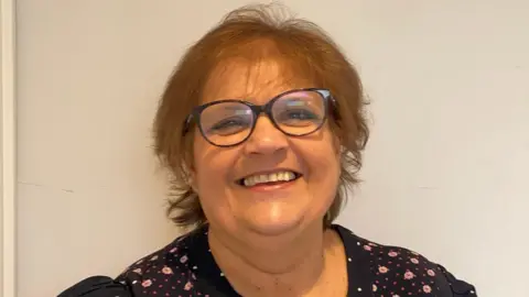 Eunice Lumsden A lady smiling with glasses on and wearing a polka dot floral navy blue dress. 