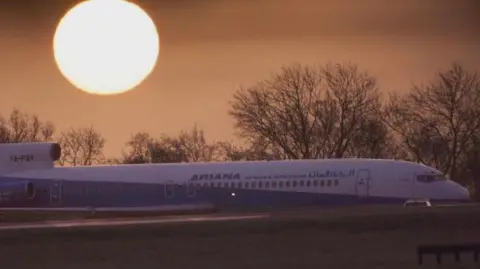 PA Media A picture of an Ariana Airlines flight at Stansted Airport with the rising sun in the background.