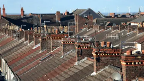 PA Media A shot of a row of terraced house roofs, with chimneys, aerials and satellite dishes on display.