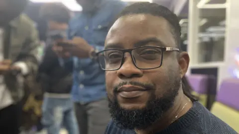 Ndukwe Onuoha wearing black glasses, sitting in the barbers shop at one of the mental health sessions