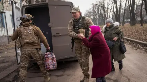 Reuters Two men in combat fatigues escorting two elderly women to a van in the Ukrainian town of Pokrovsk