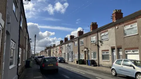 A street of houses with cars in the sunshine.