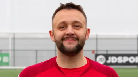 Image of Joe Brailsoford, who has brown hair, brown beard and wearing red football shirt