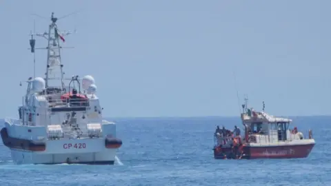 REUTERS Two boats, one mainly red and the other mainly white, in the sea. with crew members visible at the stern of the smaller (red) boat.