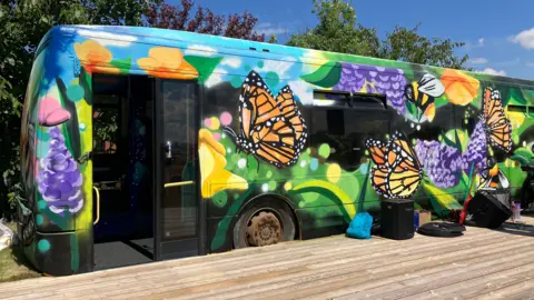 BBC An old bus that has been painted with brightly coloured flowers and butterflies