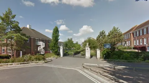 Google Google Street View of Thomas Hardye School in Dorchester. Two storey red brick buildings are arranged around a garden behind stone pillars and metal gates.