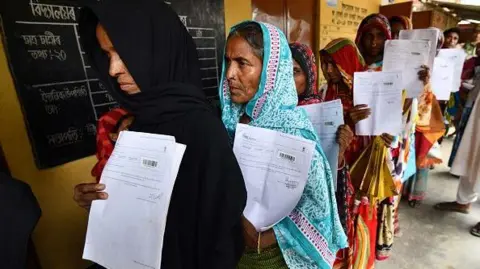 Getty Images Residents hold their documents as they stand in a queue to check their names on the final list of National Register of Citizens (NRC) at a NRC Sewa Kendra (NSK) in Burgoan village in Morigoan district on July 30, 2018