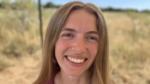 Woman smiling at the camera, she has long ash blonde hair and blue eyes
