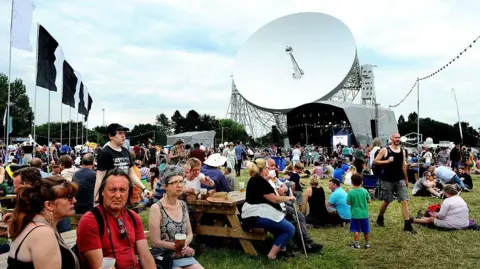 Getty Images The Lovell Telescope looms large over a festival stage, with lots of the audience sitting and standing in front of it