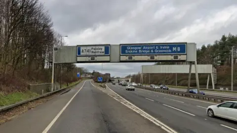 Motorway and slip road with blue and white overhead signs saying junction 27 and with a number of destinations and M8 written in white or black 