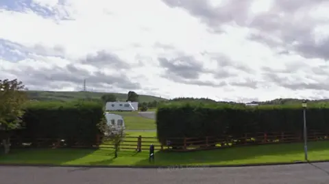 A green field with hedges at the boundary and white caravans in the distance. 