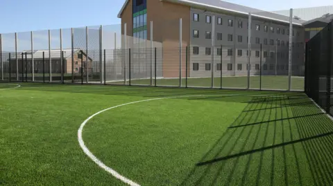 Getty Images A football pitch at HMP Berwyn. An Astroturf surrounded by a white metal fence is overlooked by a prison building behind it.