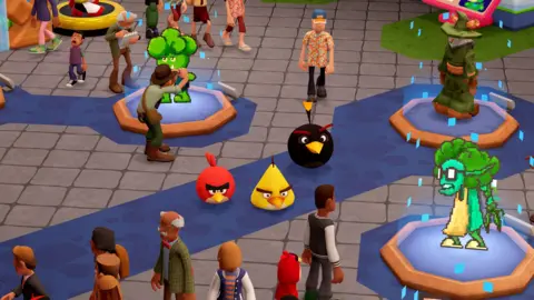 Sega A still from the Two Point museum games shows players walking around a museum setting with a blue carpet and displays. Each display has a blue base and green character. There are children, animals and adults of different ages in the scene 
