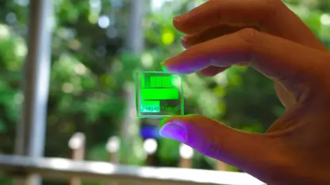 Helio A hand holding a clear plastic square with helio's green perovskite colour converter film on top