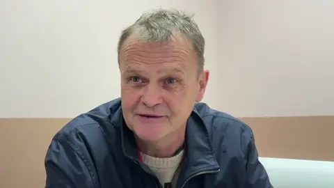 Billy Knight has short grey hair, a blue jacket and light jumper. He is sat in a room.