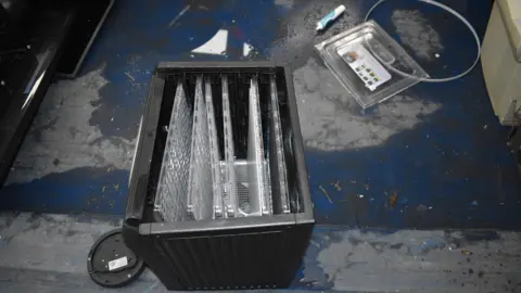 Supreme Court of Victoria Dehydrator pictured at the tip, where it was recovered from. It is standing on its back (the opening is facing up) and the door to it is on the floor behind. There are other unidentifiable objects near it.