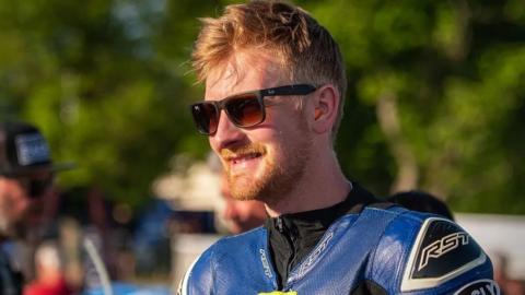 A man smiling with sunglasses in a blue TT racing suit