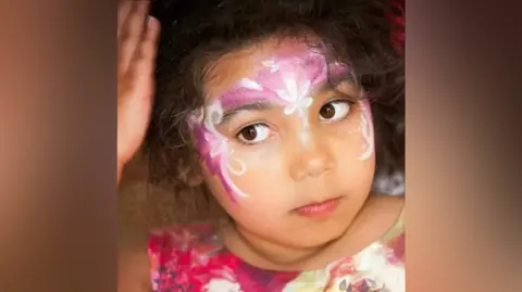 Beverley Williams Amira when she was younger in pink face paint and a pink top.