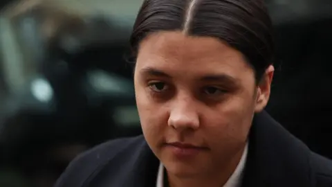 Sam Kerr arriving at court in a suit, looking serious