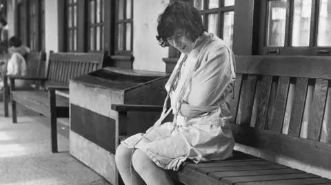 Getty Images A black and white image of a woman in a straight jacket sat on a bench